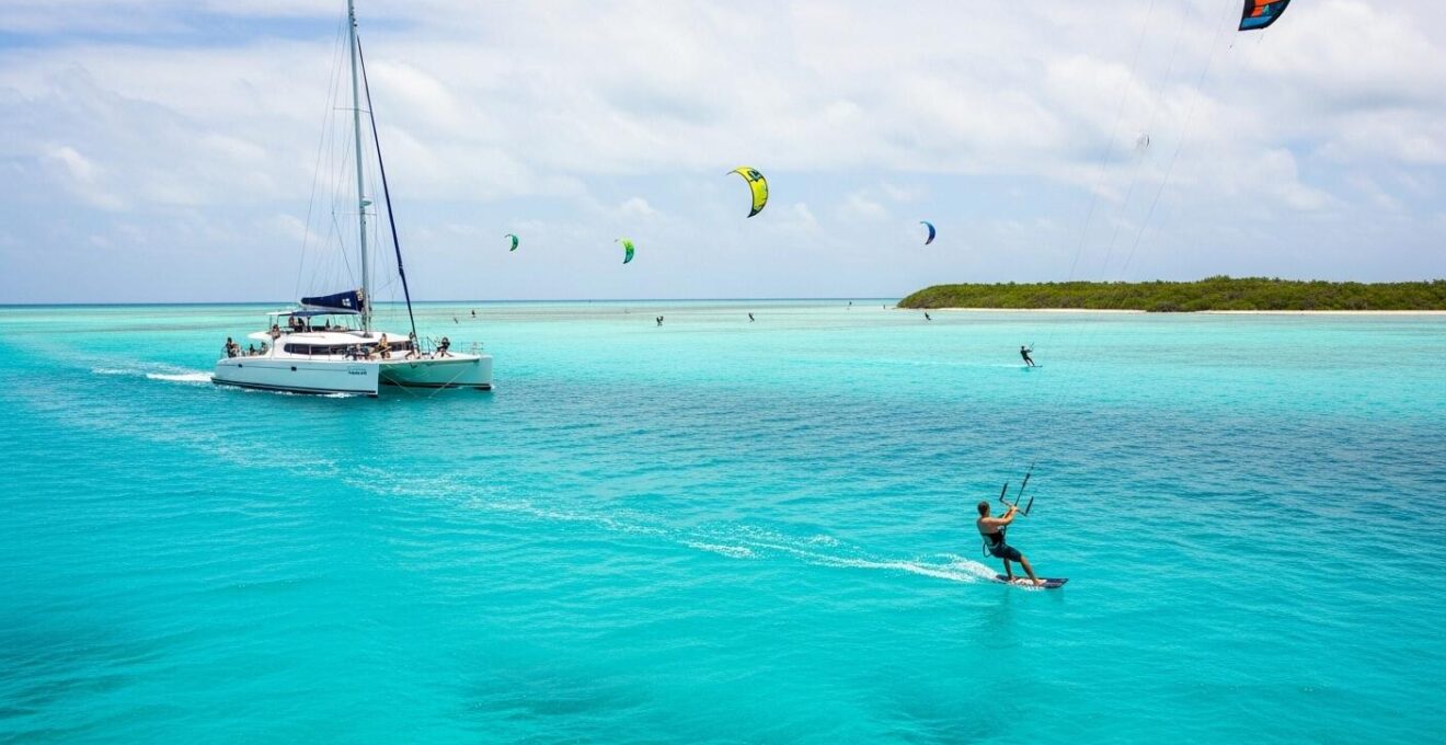 Photographie réaliste d'un catamaran kitesurf naviguant sur des eaux turquoise avec plusieurs kitesurfeurs en action, entouré d'îlots des Grenadines